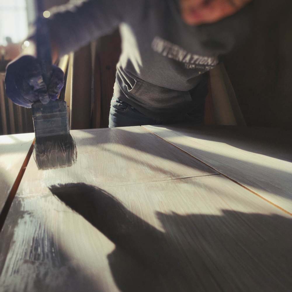 Manos restaurando con brocha una mesa de madera en la casa de Reconstrucción Generativa